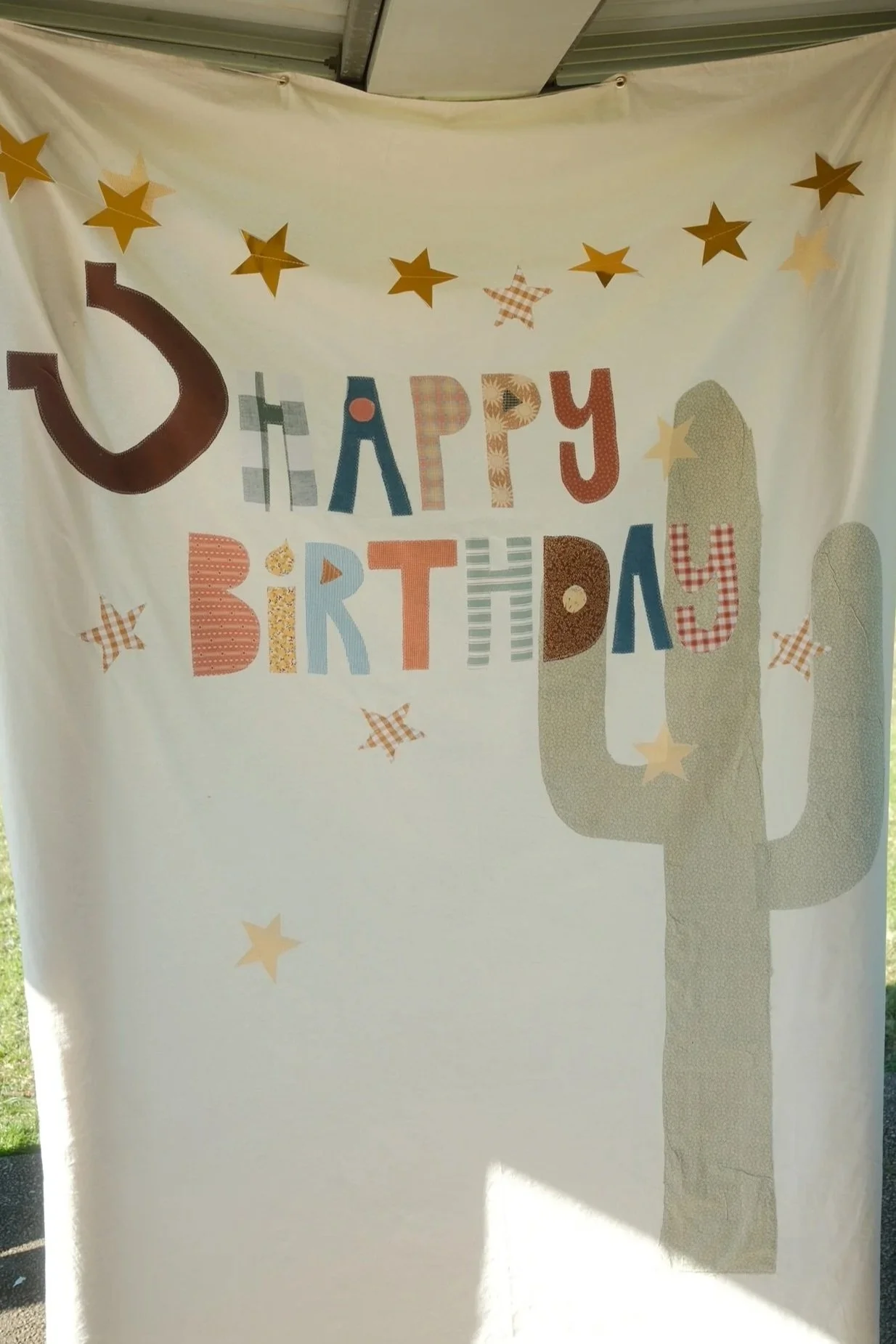 A birthday banner with colorful letters and star decorations, partially obscured by a tree shadow.