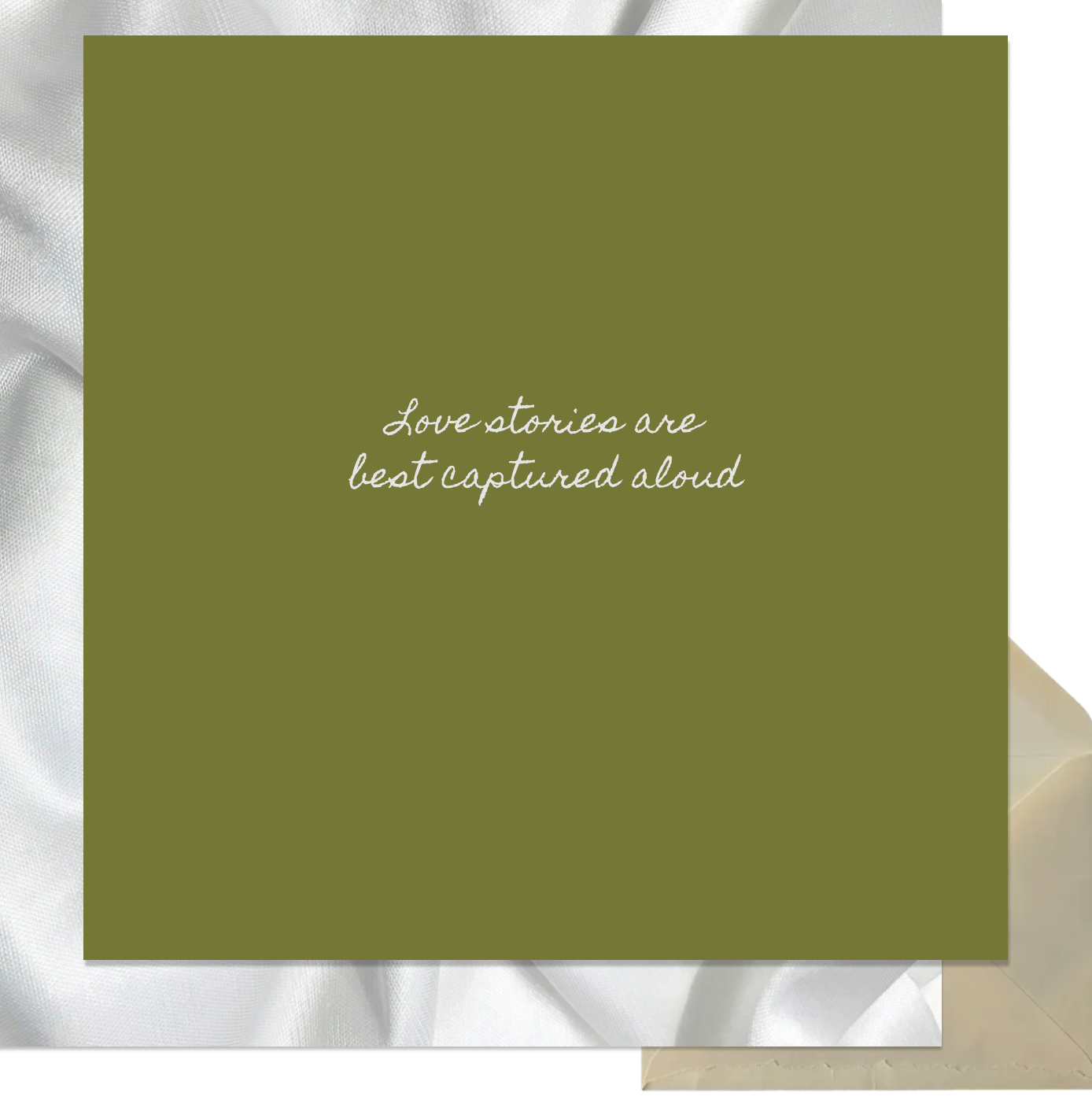 A green square with white cursive text that reads, "Love stories are best captured aloud," on top of a background with white satin fabric and part of a cream-colored envelope.