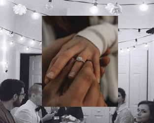 Close-up of two hands with wedding rings, with strings of lights and guests in the background