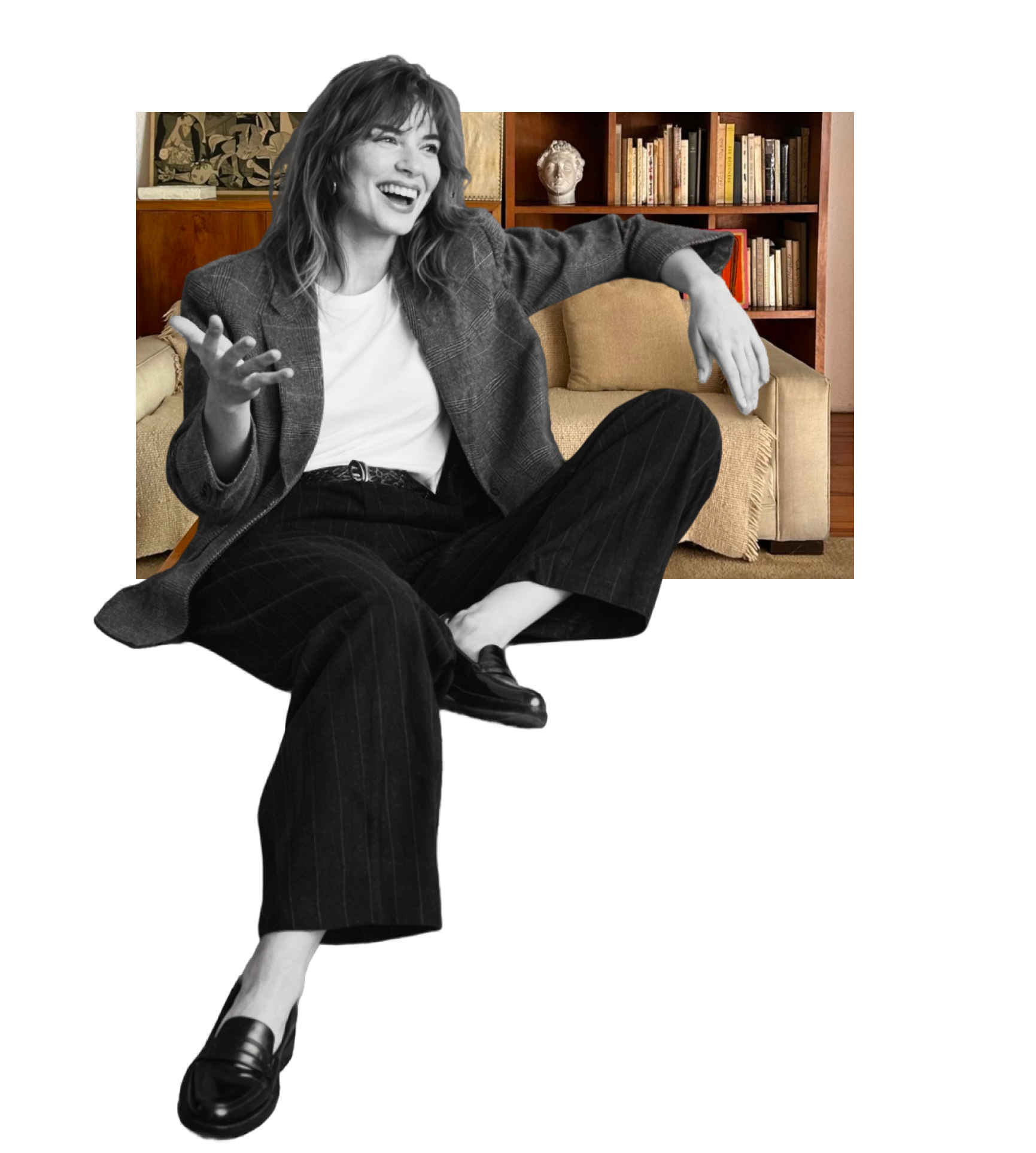 Woman sitting on edge of a sofa, laughing and gesturing with hands, in a room with a bookshelf and decorative items in the background.