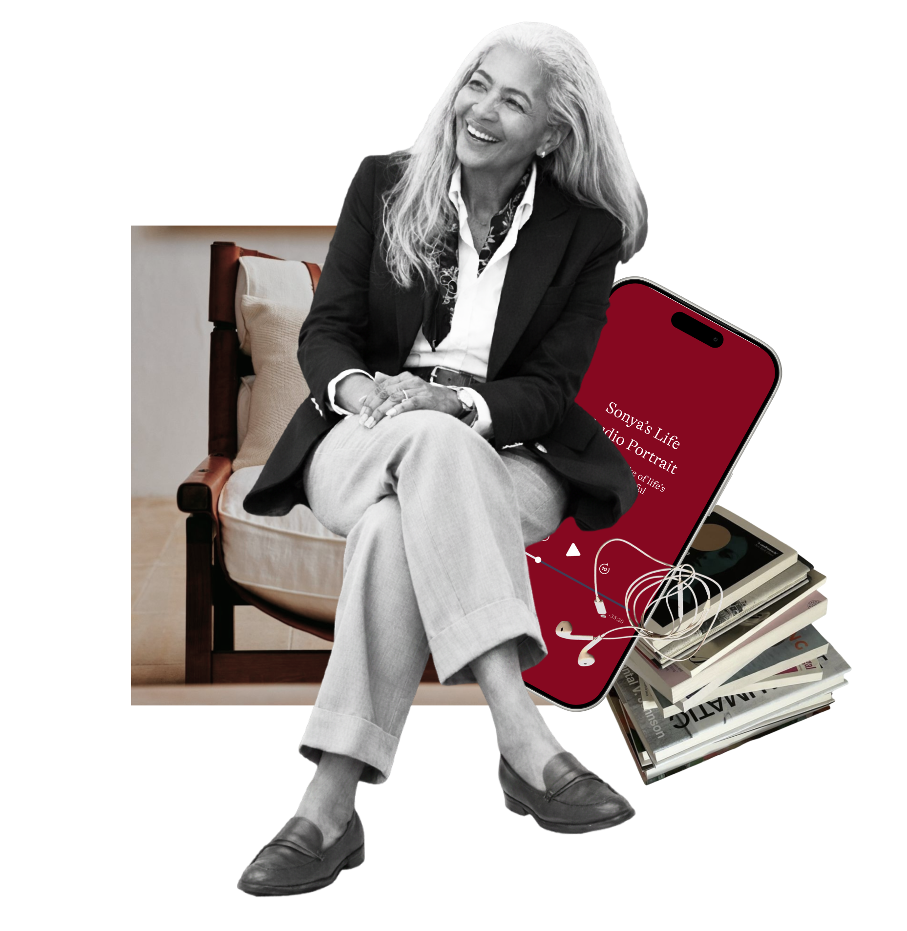 A woman with gray hair sitting on a wooden chair, smiling. She is dressed in a black blazer, white shirt, and light-colored pants. There are books and a smartphone with earbuds next to her.