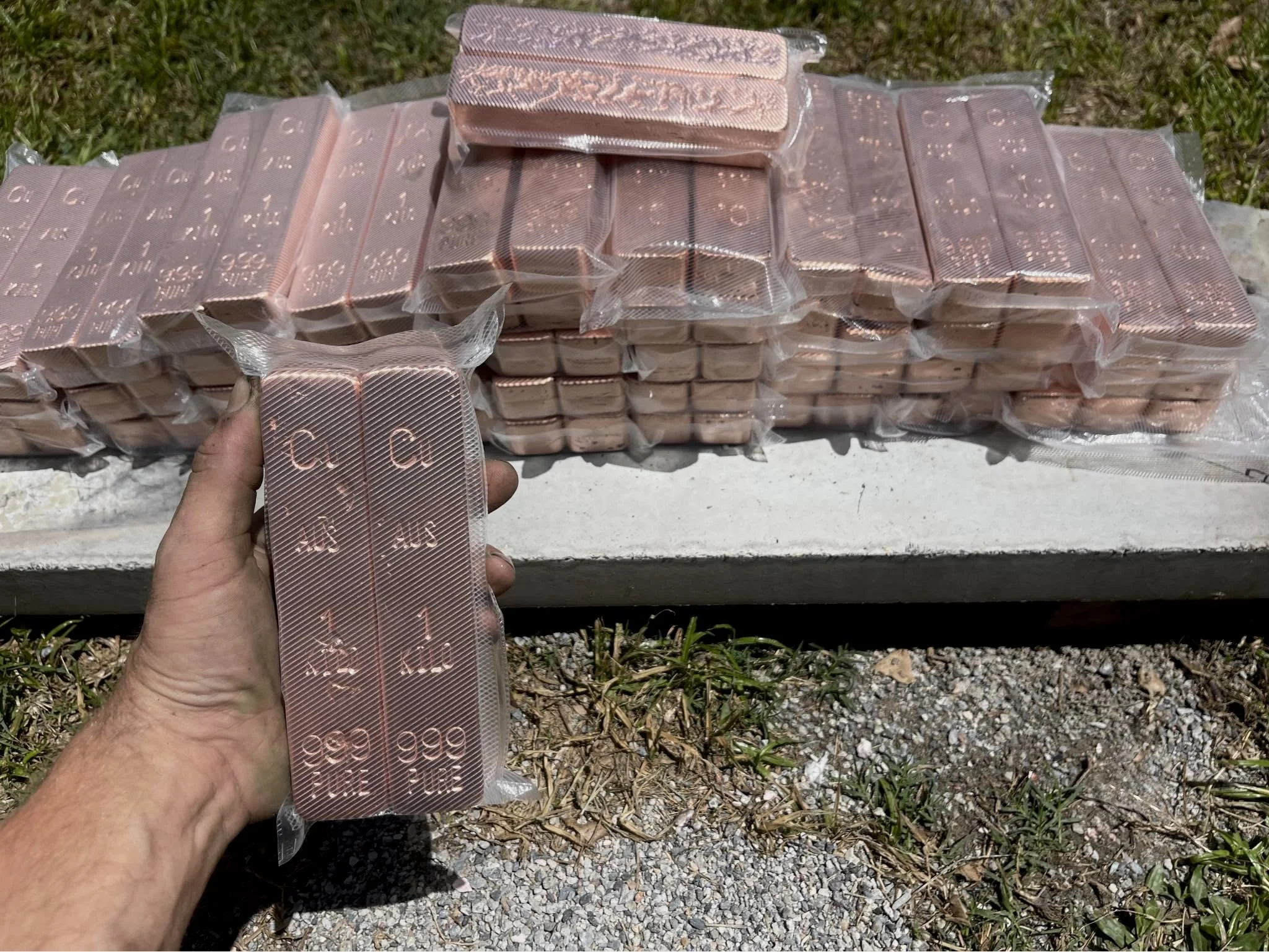 Hand holding 1kg copper bullion bar with stacked bars in background 999 fine Australia