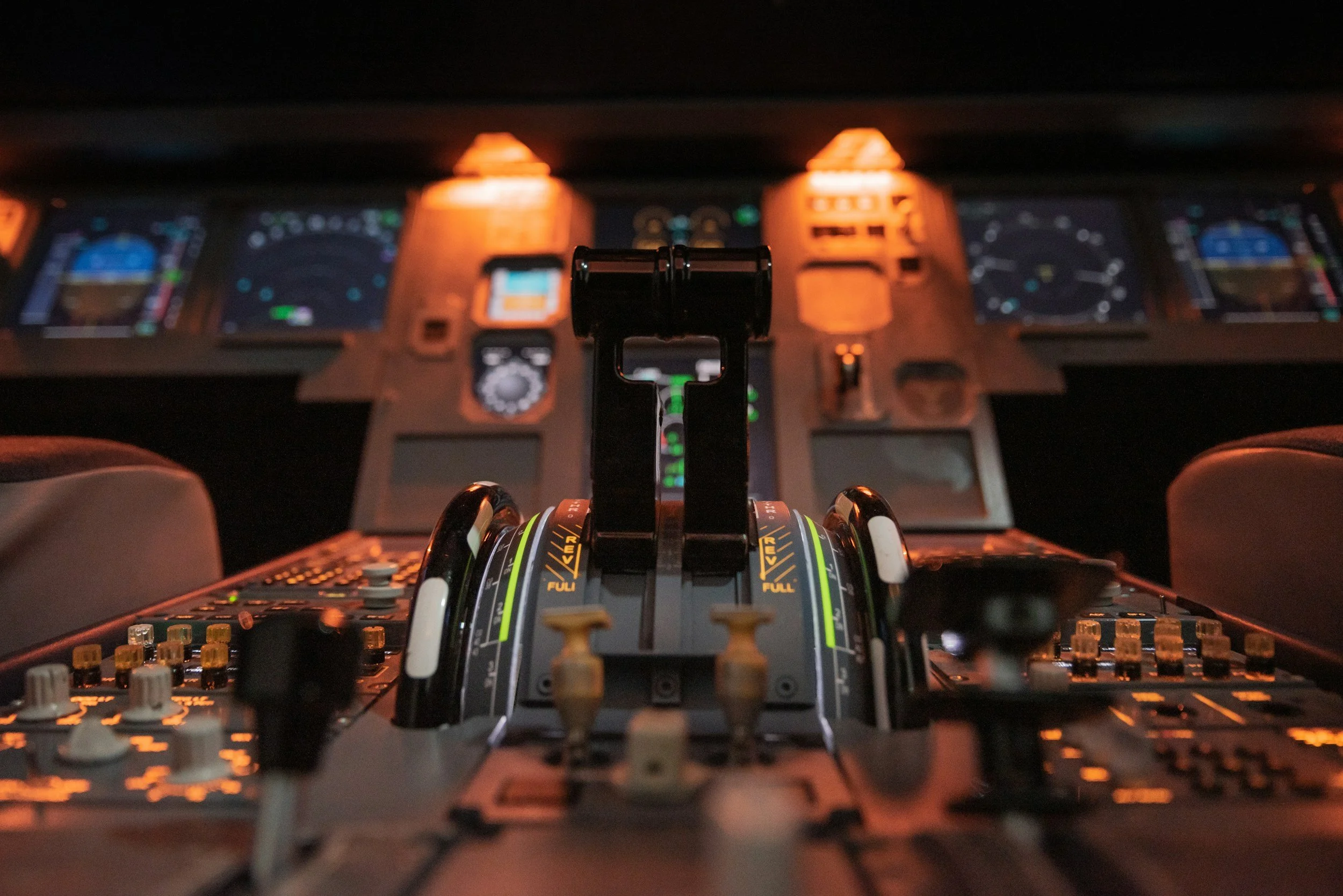 Close-up of an airplane cockpit's throttle and control panel with illuminated instruments and screens.