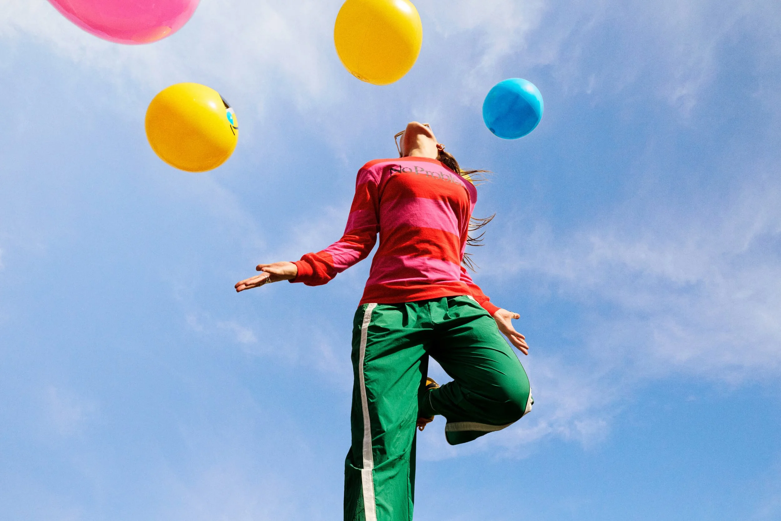 Person balancing on one leg outdoors under a blue sky with colorful balloons floating above.