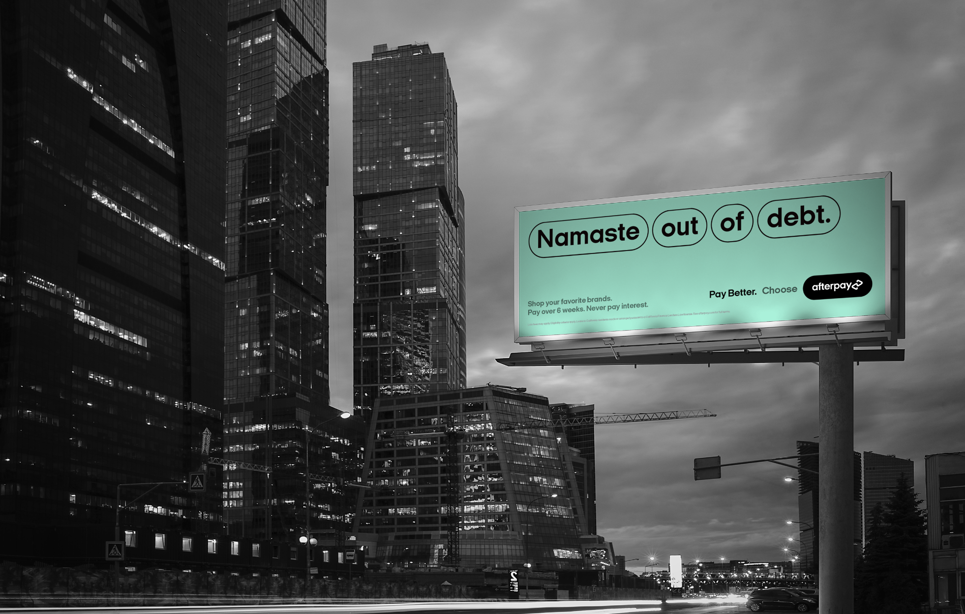 A billboard displays the text 'Namaste out of debt' against a city skyline in black and white. The billboard has a green background with the words 'Namaste', 'out', 'of', and 'debt' enclosed in oval shapes. Additional smaller text promotes shopping and payment options.