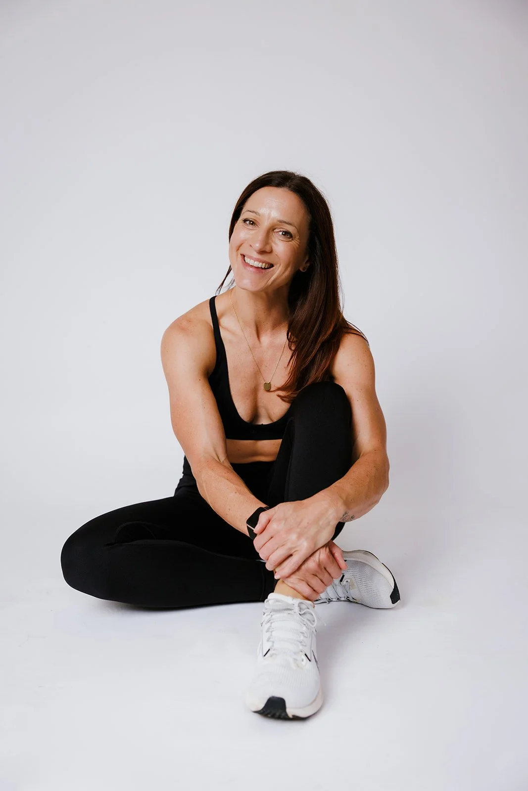 A picture of Nicole Hauxwell in workout clothes sitting on the floor and smiling.
