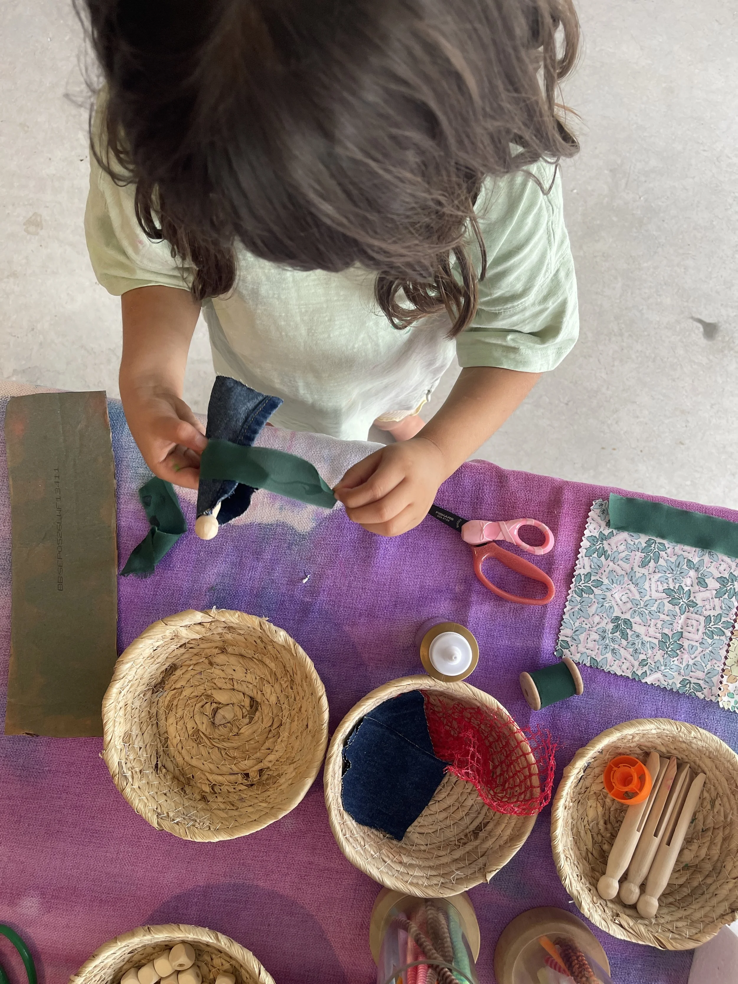 Child dressing a wooden peg doll in denim and fabric scraps as part of a process art tinker table activity