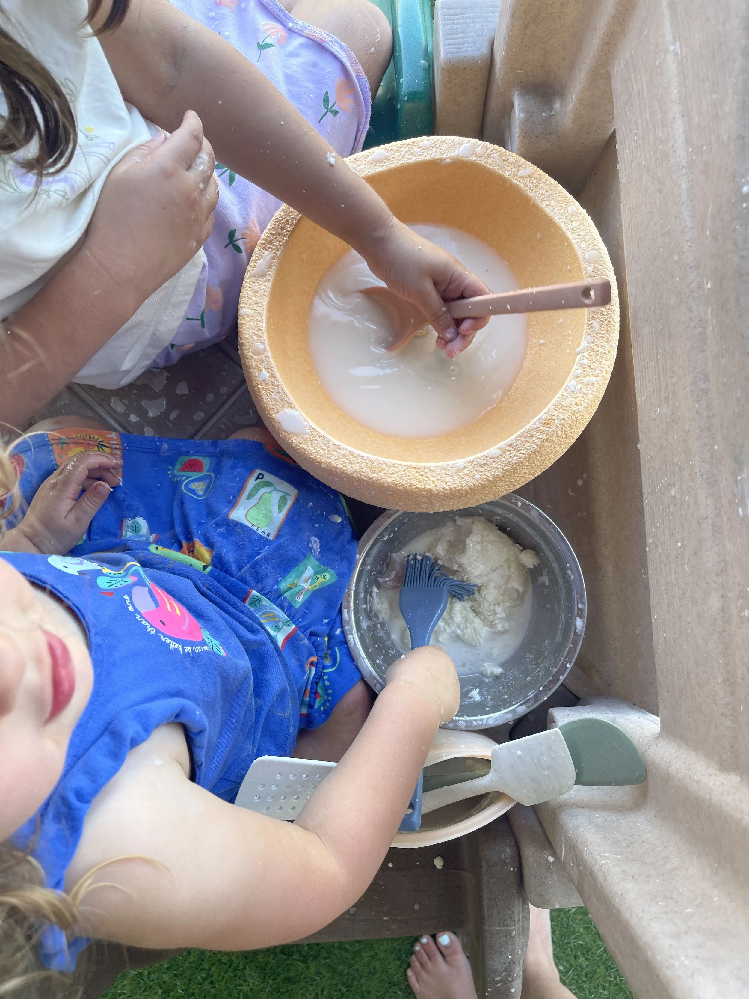 Two toddlers mixing water and dough in kitchen bowls as part of a hands-on sensory play station