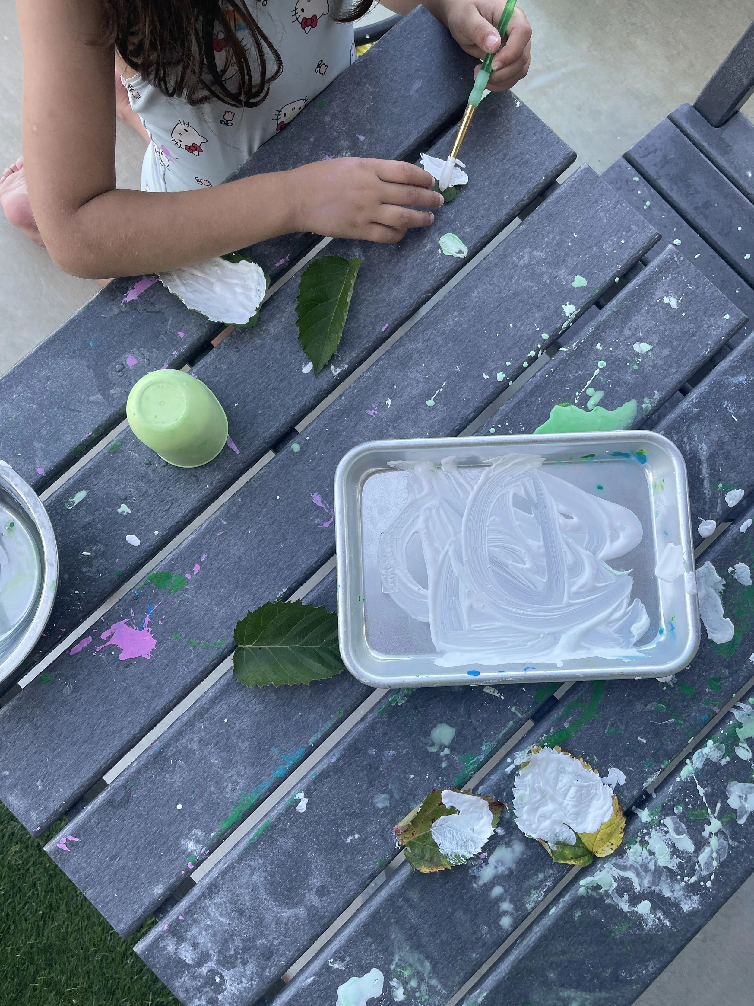 Toddler using a basting brush to paint a leaf for a no-prep nature process art activity