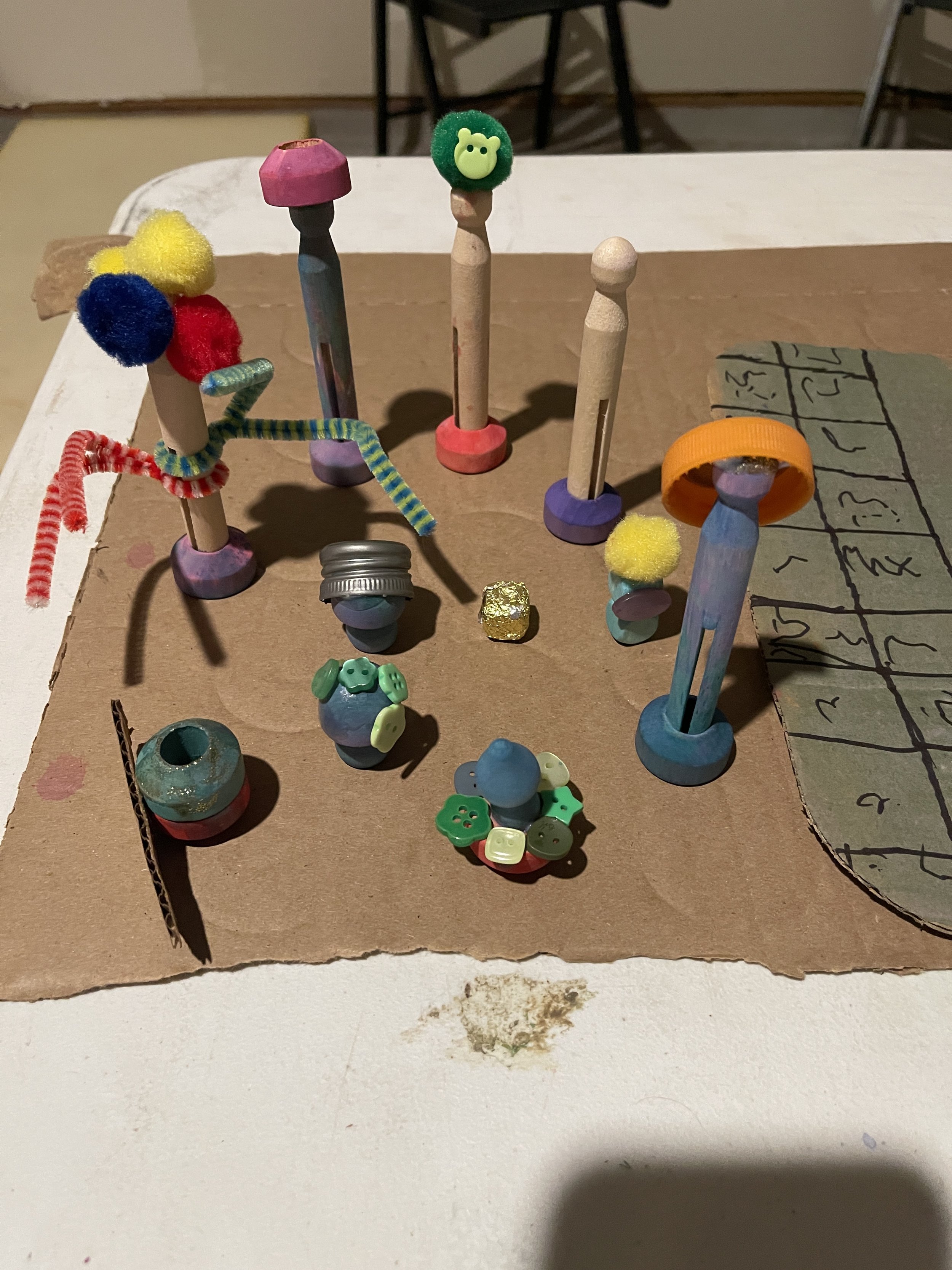 A child's cardboard game board and figures using loose parts and recycled materials