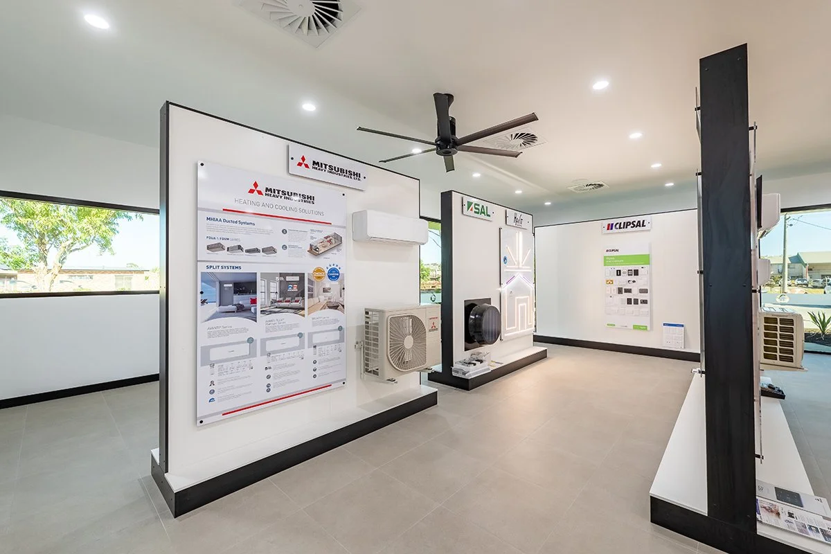 Showroom with HVAC systems displays, Mitsubishi, SAL, and Clipsal branding, air conditioning units, fans, and diagrams on posters