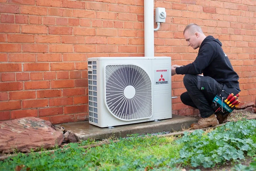 A technician working on an outdoor air conditioning unit next to a brick wall.