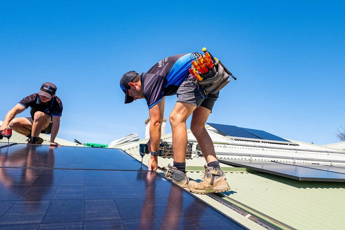 Workers installing solar panels on a roof under a clear blue sky.