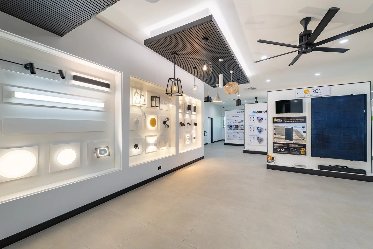 Interior showroom displaying various lighting fixtures, ceiling fans, solar panels, and electronic displays on white walls with modern decor.