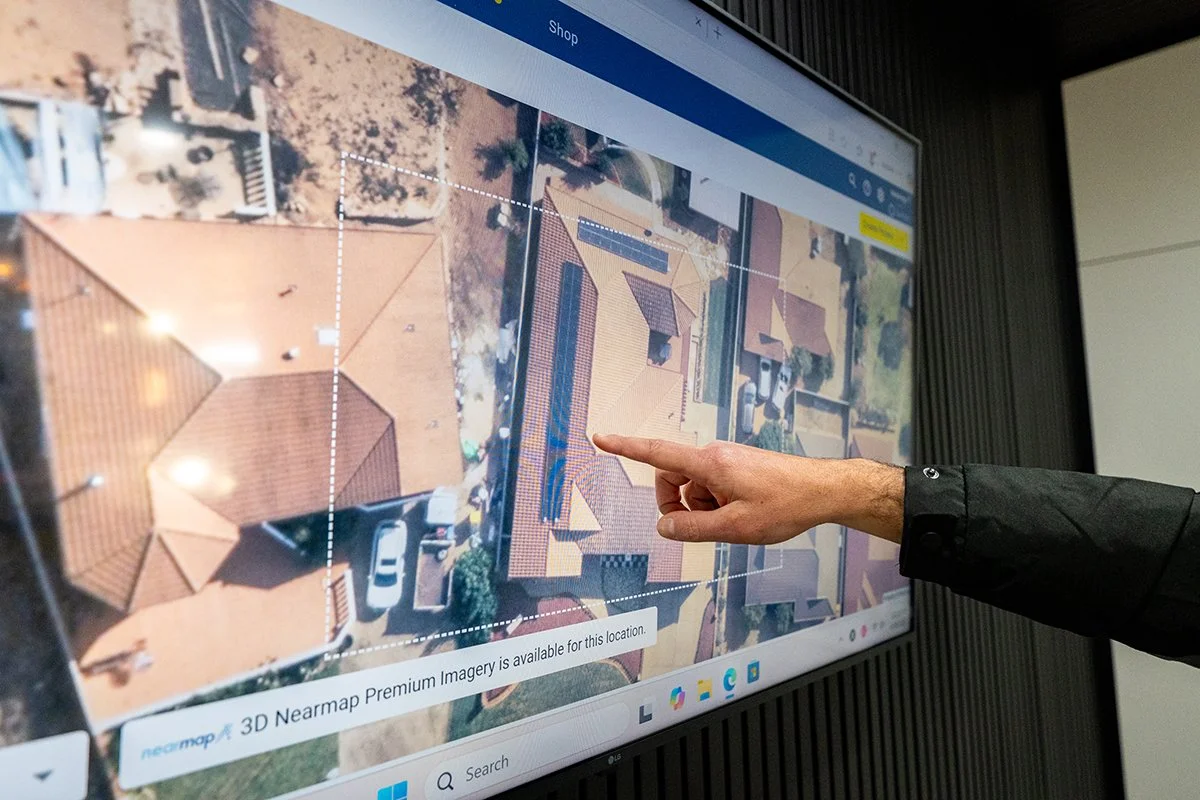 Person pointing at a house with solar panels on the roof displayed on a large digital map screen.