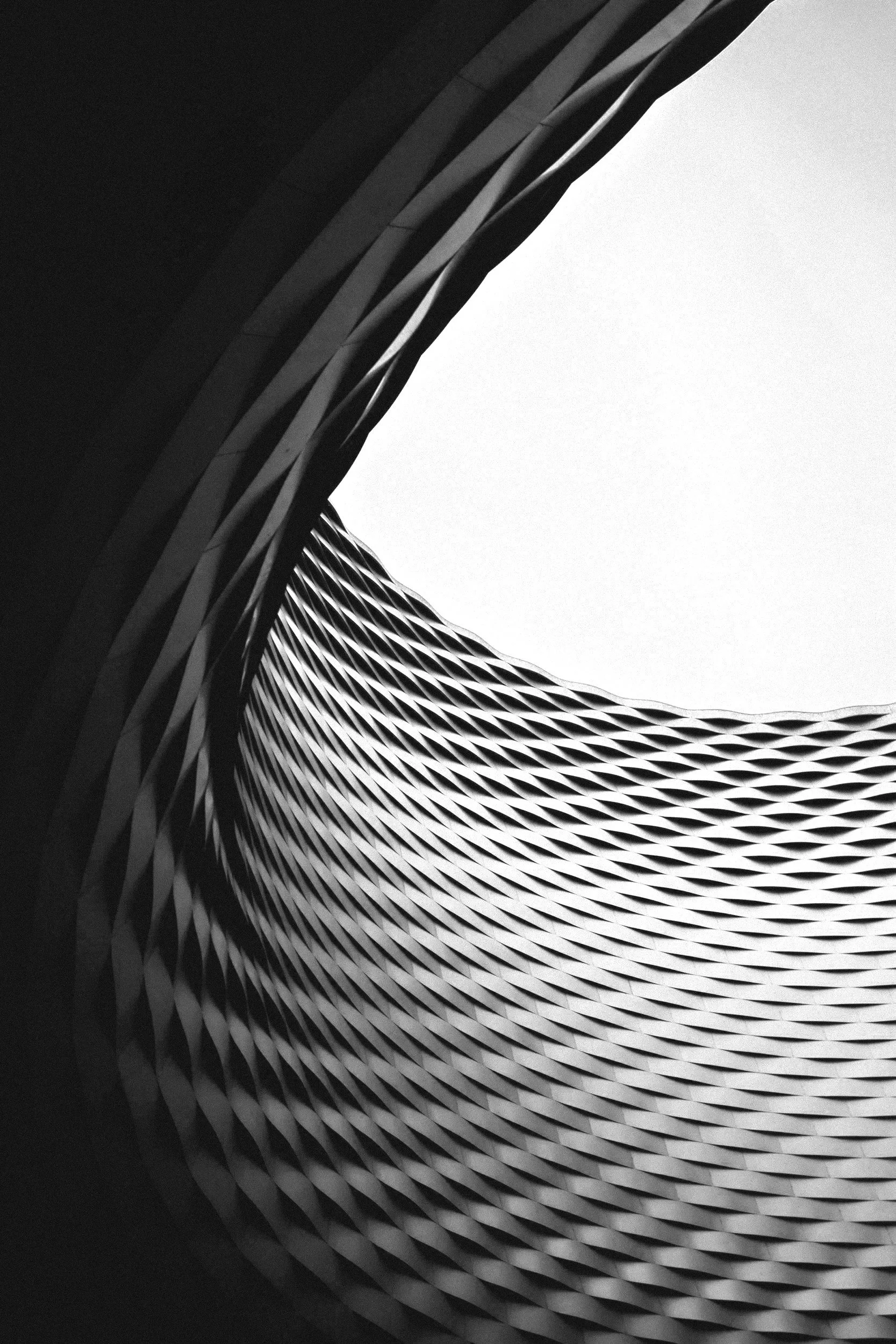 Close-up view of a modern architectural structure with woven or textured metal panels forming a curved surface, taken from below looking up.