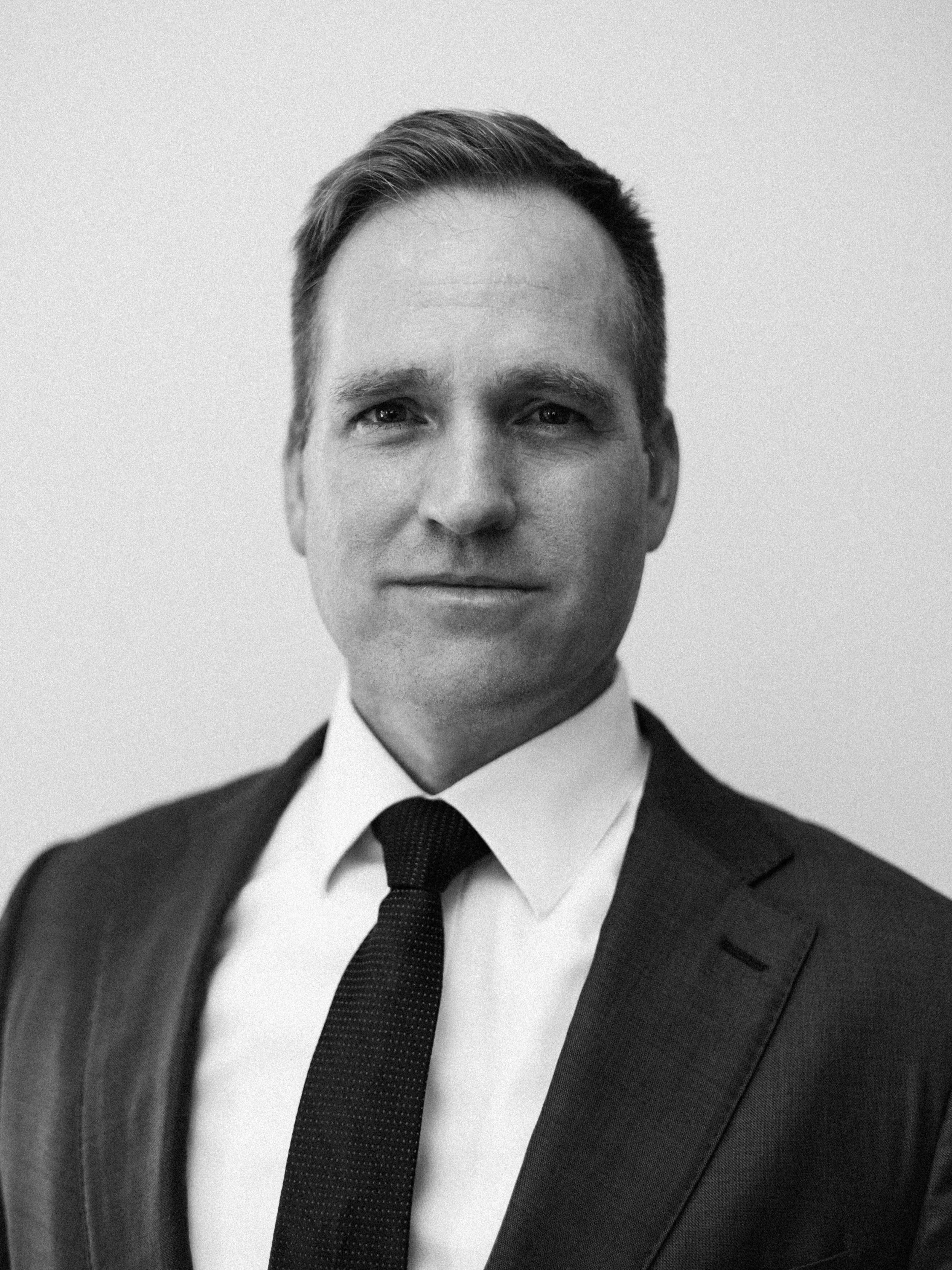 Black and white portrait of a man in a suit and tie, facing forward with a neutral expression.