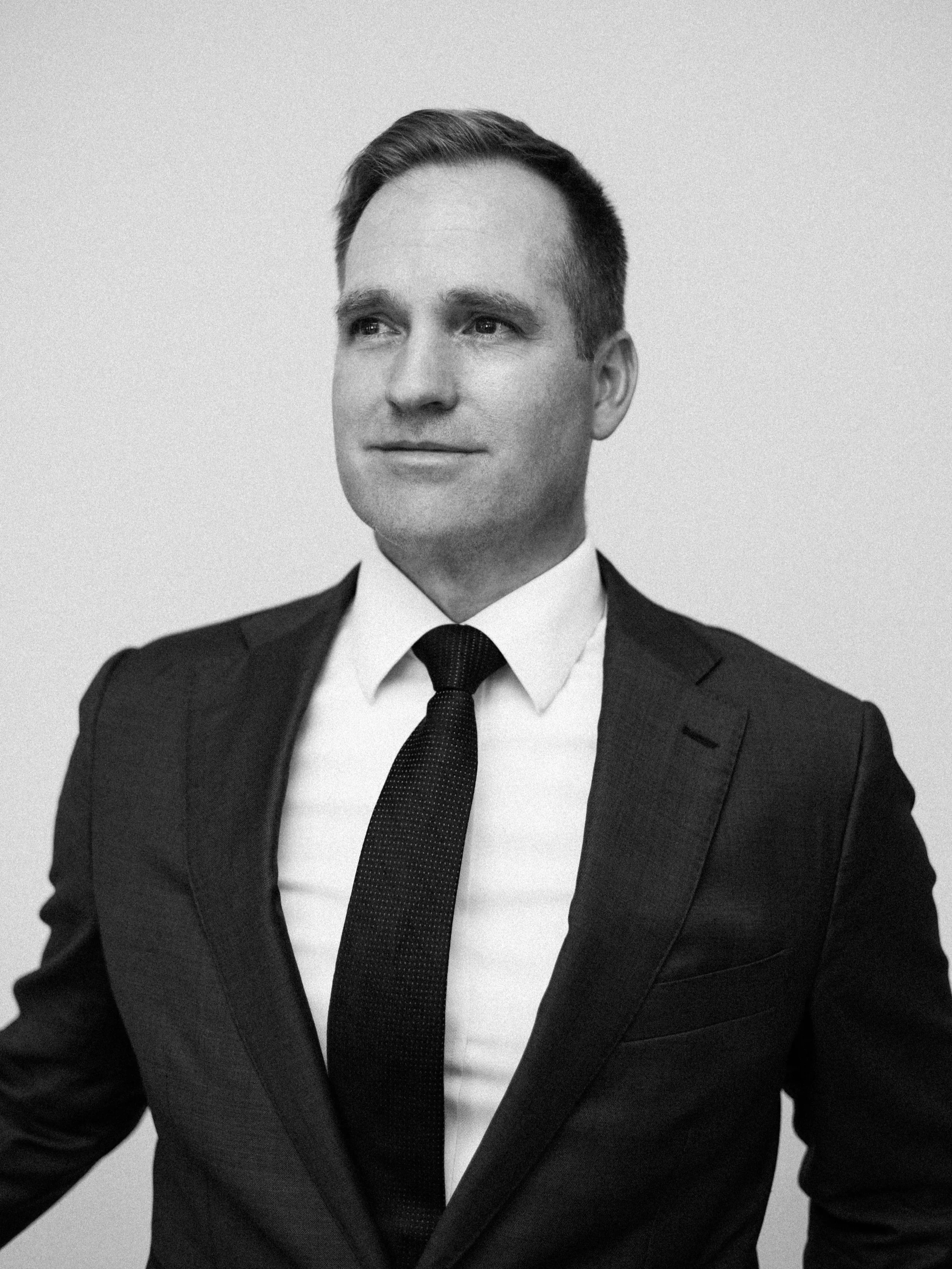 Black and white portrait of a man in formal business attire, with a suit, white shirt, and tie, looking slightly to the side.