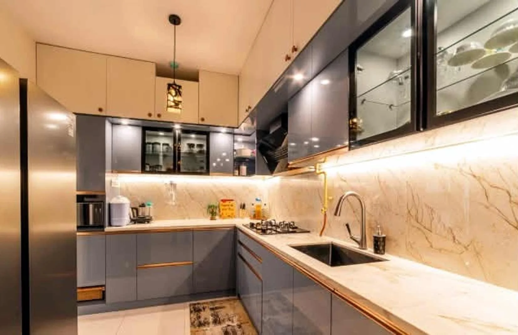 "High-gloss white modular kitchen design with a mirrored backsplash, built-in breakfast bar, and stainless steel hardware."