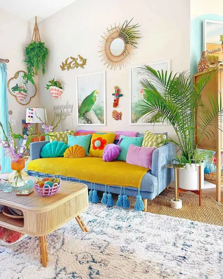 Bright living room with a cream-colored fabric sofa, large indoor monstera plant, and natural sunlight streaming through sheer curtains."