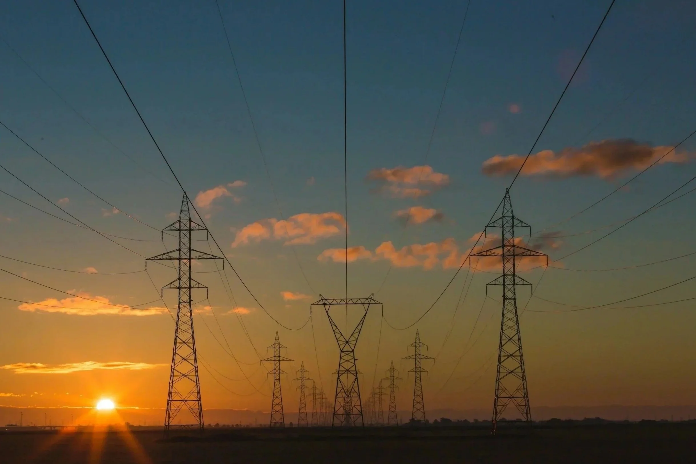 Sunset over power lines and transmission towers in a rural landscape.