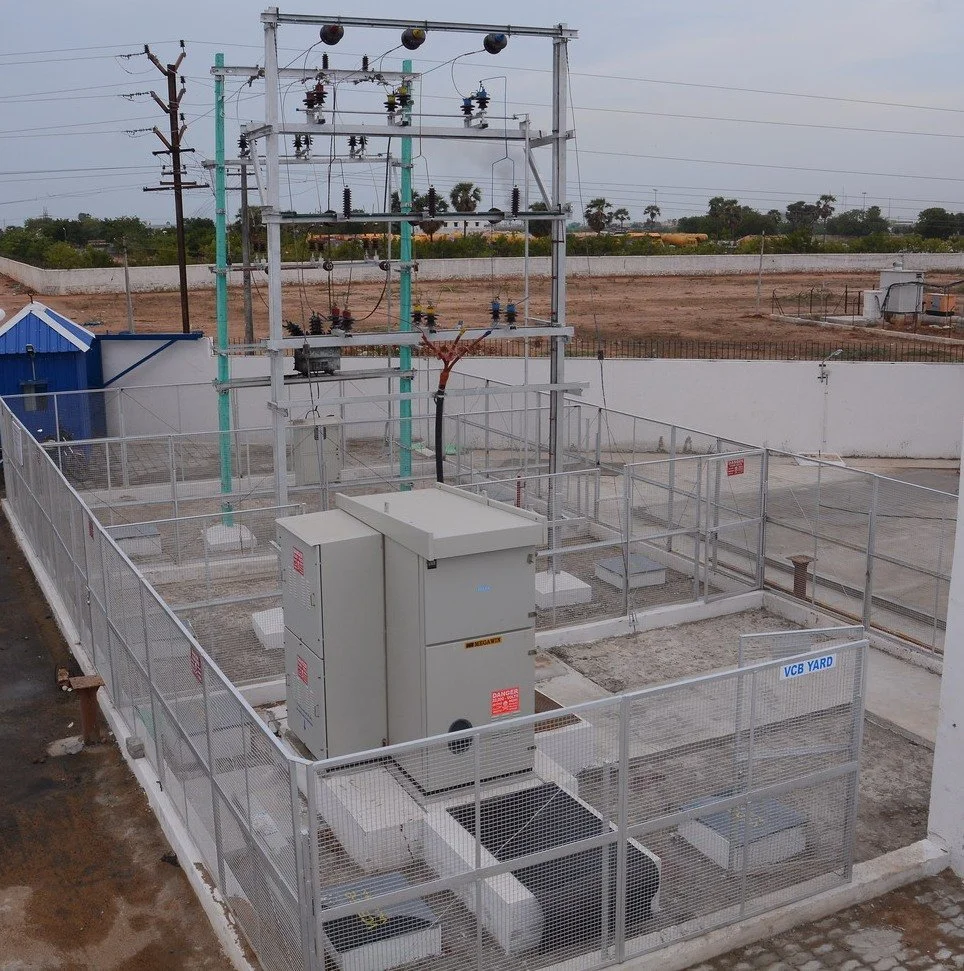 An outdoor electrical substation with power lines, equipment, and fencing.