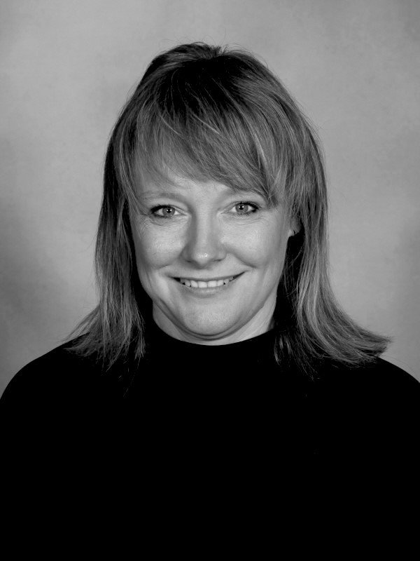 Black and white portrait of a woman with shoulder-length hair, smiling, wearing a dark top, against a plain background.