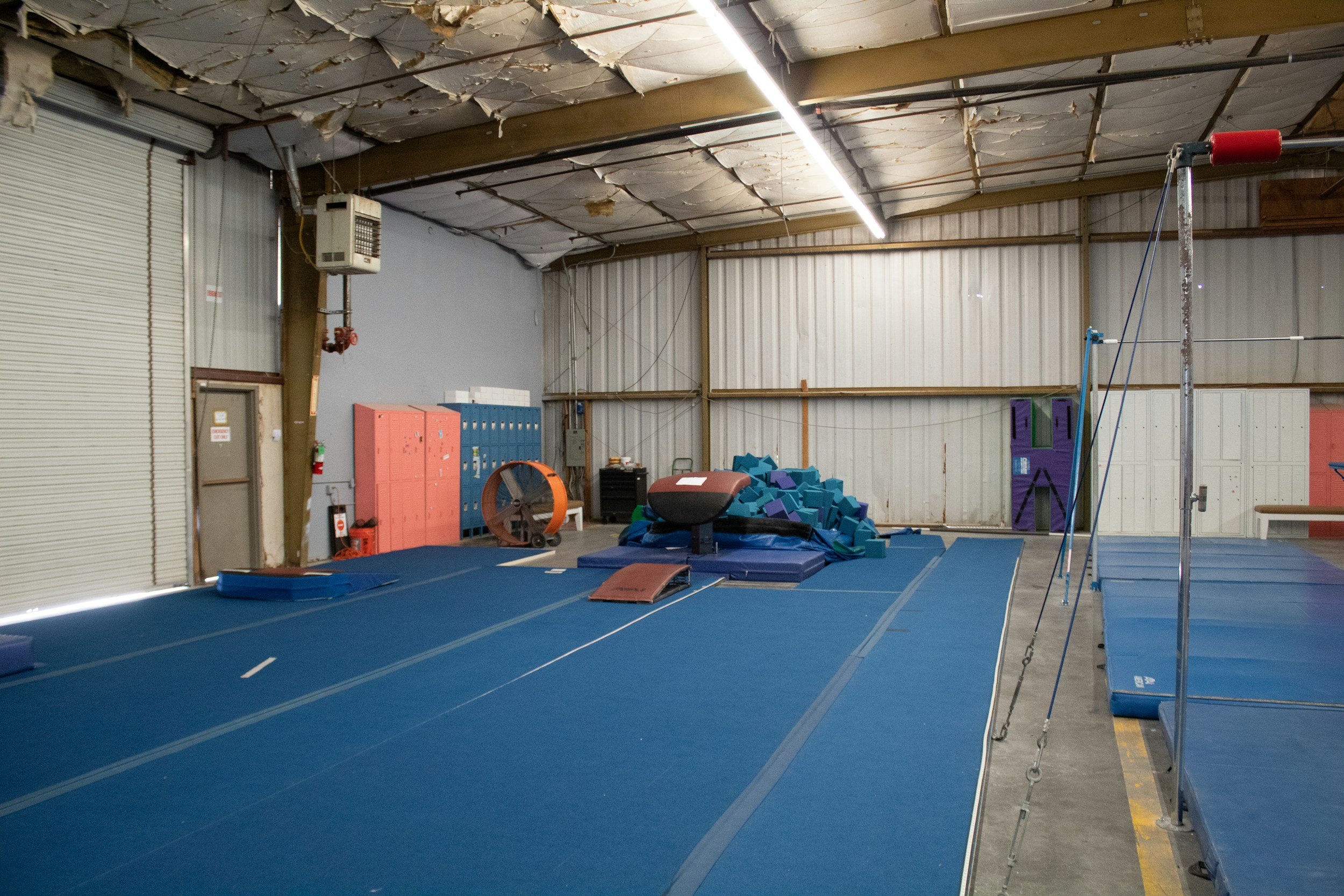 Indoor gymnastics training area with blue mats, vaulting equipment, foam blocks, and a swing frame.