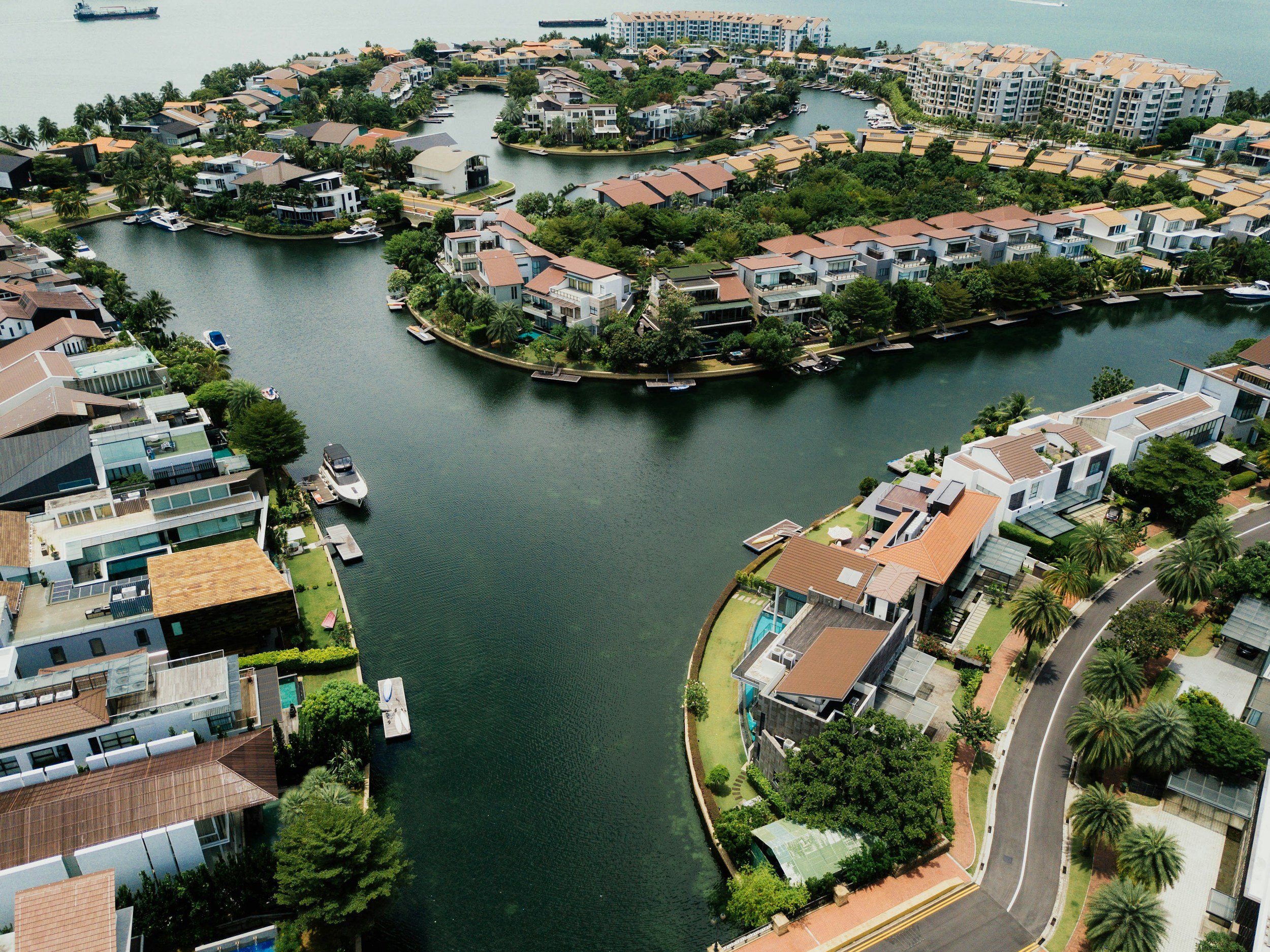 Aerial view of a residential waterfront community with houses along winding canals, lush greenery, palm trees, and boats docked at the water's edge.
