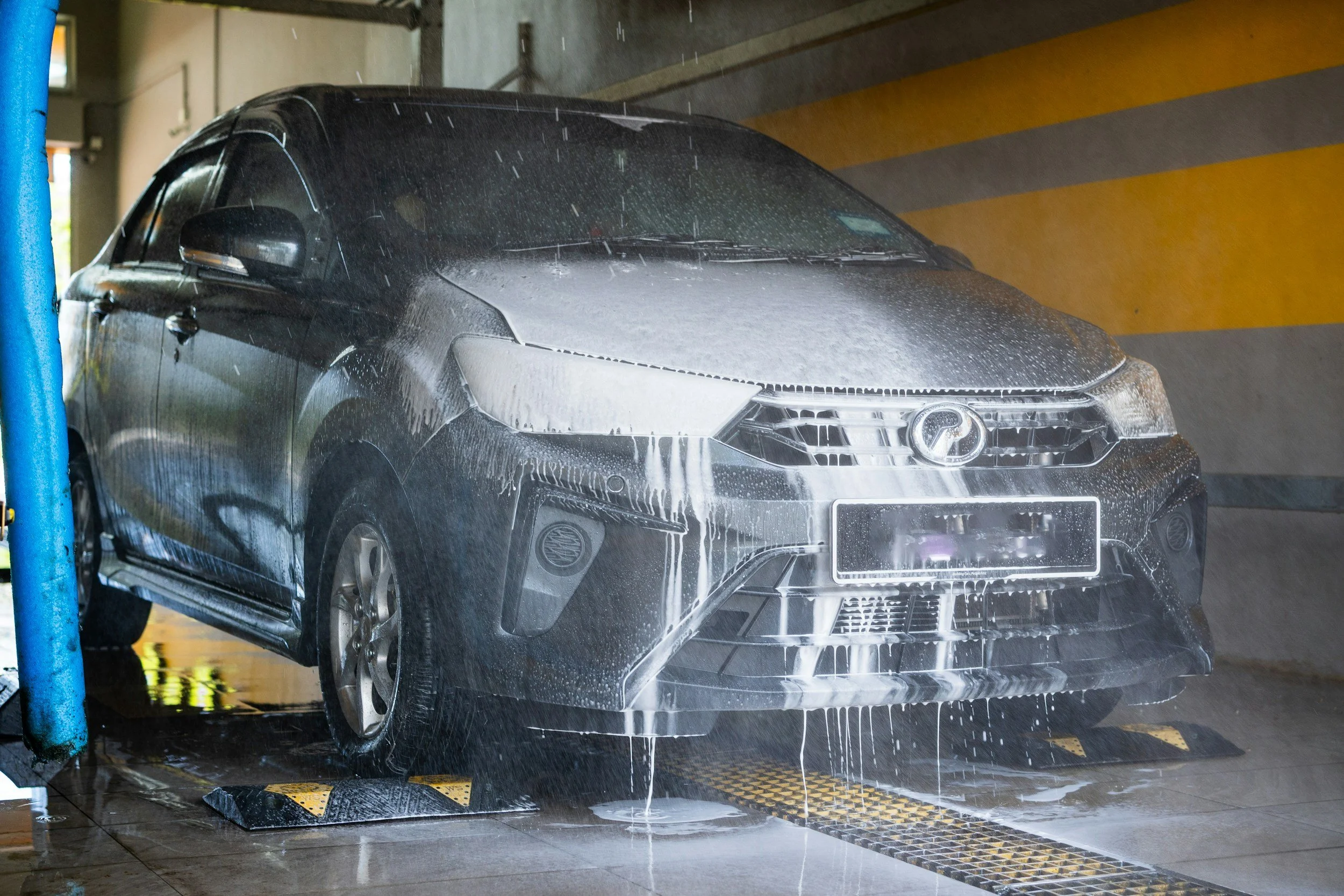 Black car being washed with foam at an automatic car wash station.
