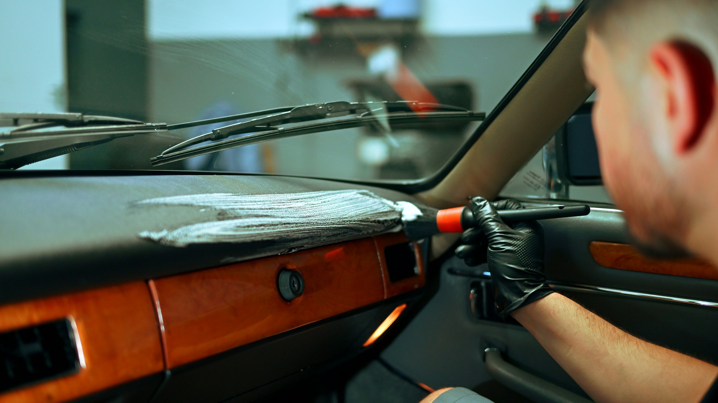 A person cleaning or repairing the dashboard of a vehicle using a tool while wearing black gloves.
