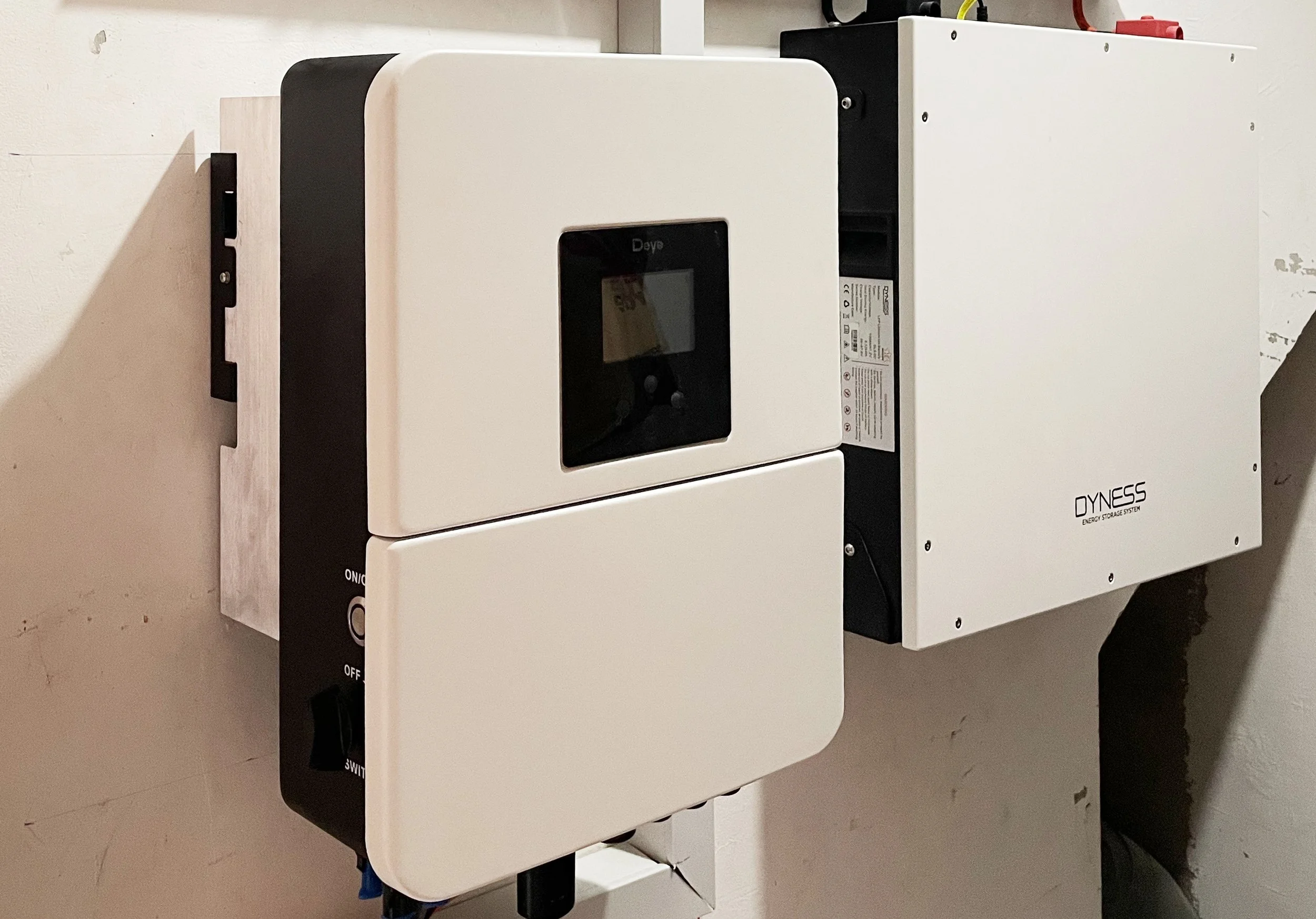 A split energy storage system mounted on a wall, with a black control panel on the left and white units on the right, labeled Dyness.