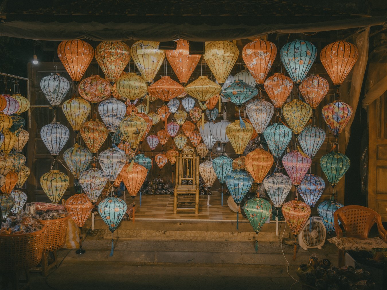 Colorful paper lanterns hanging at night, decorated with floral and nature patterns, displayed in a shop or market setting.