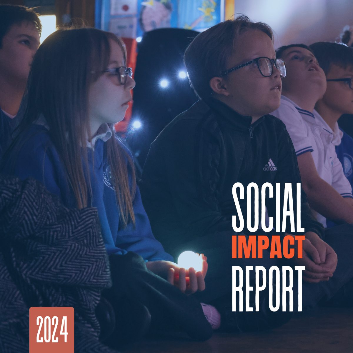 Cover image for the 2024 Social Impact Report showing children watching an interactive light-based activity in a classroom.