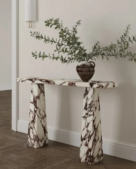 Marble console table with a vase and green leafy branches against a white wall.