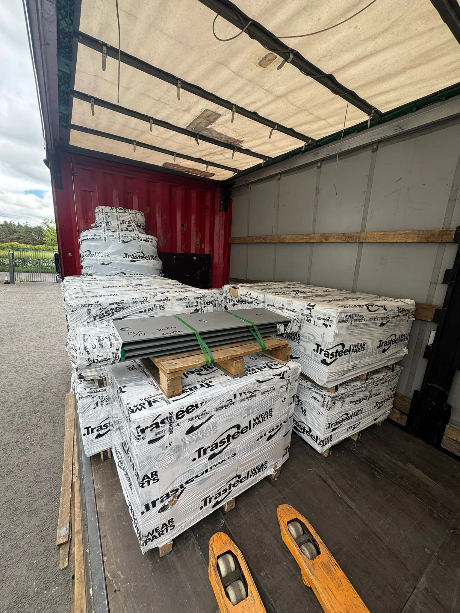 Interior of a delivery truck with wrapped car parts, stacked on pallets, and a set of orange hand trucks on the floor.