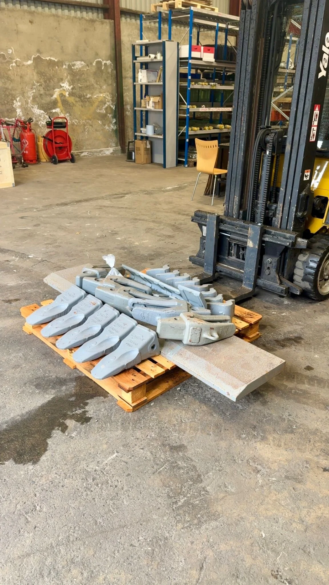 Forklift in a warehouse with metal parts on a wooden pallet and a concrete floor.