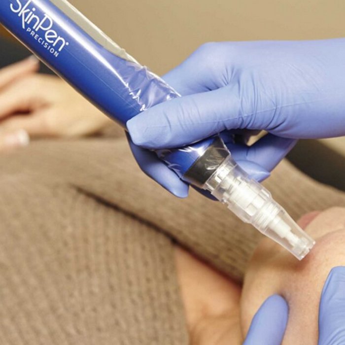 A healthcare professional wearing blue gloves administering an injection to a person's arm using a medical syringe and a blue pen-like device.
