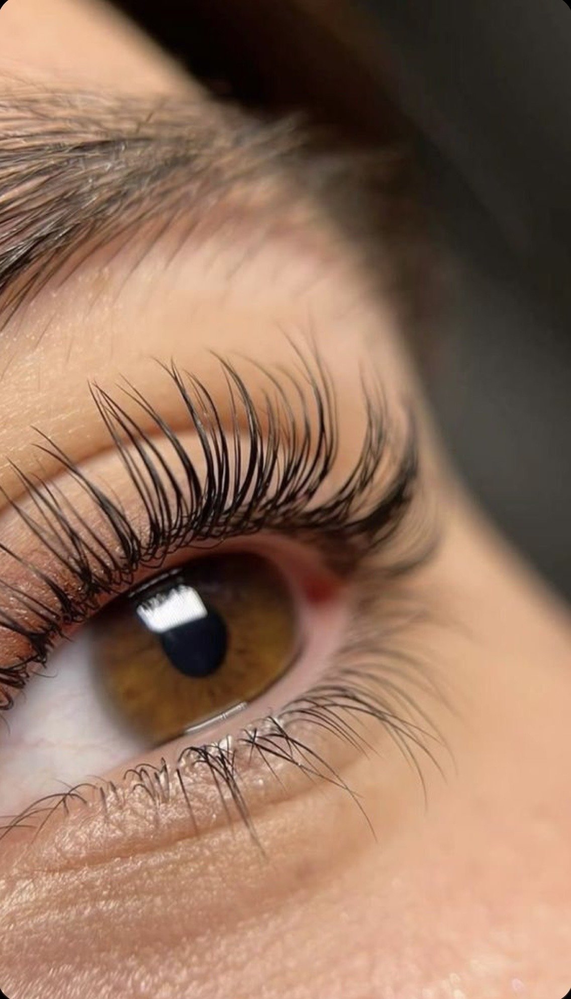 Close-up of a human eye showing brown iris, long eyelashes, and smooth skin around the eye.
