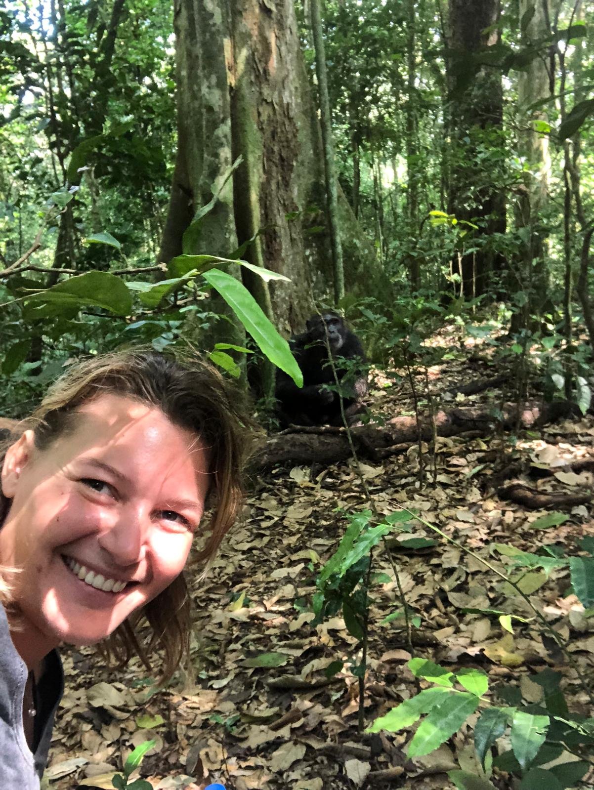 Photo dans la forêt avec une femme souriante et un chimpanzé assis sur le sol