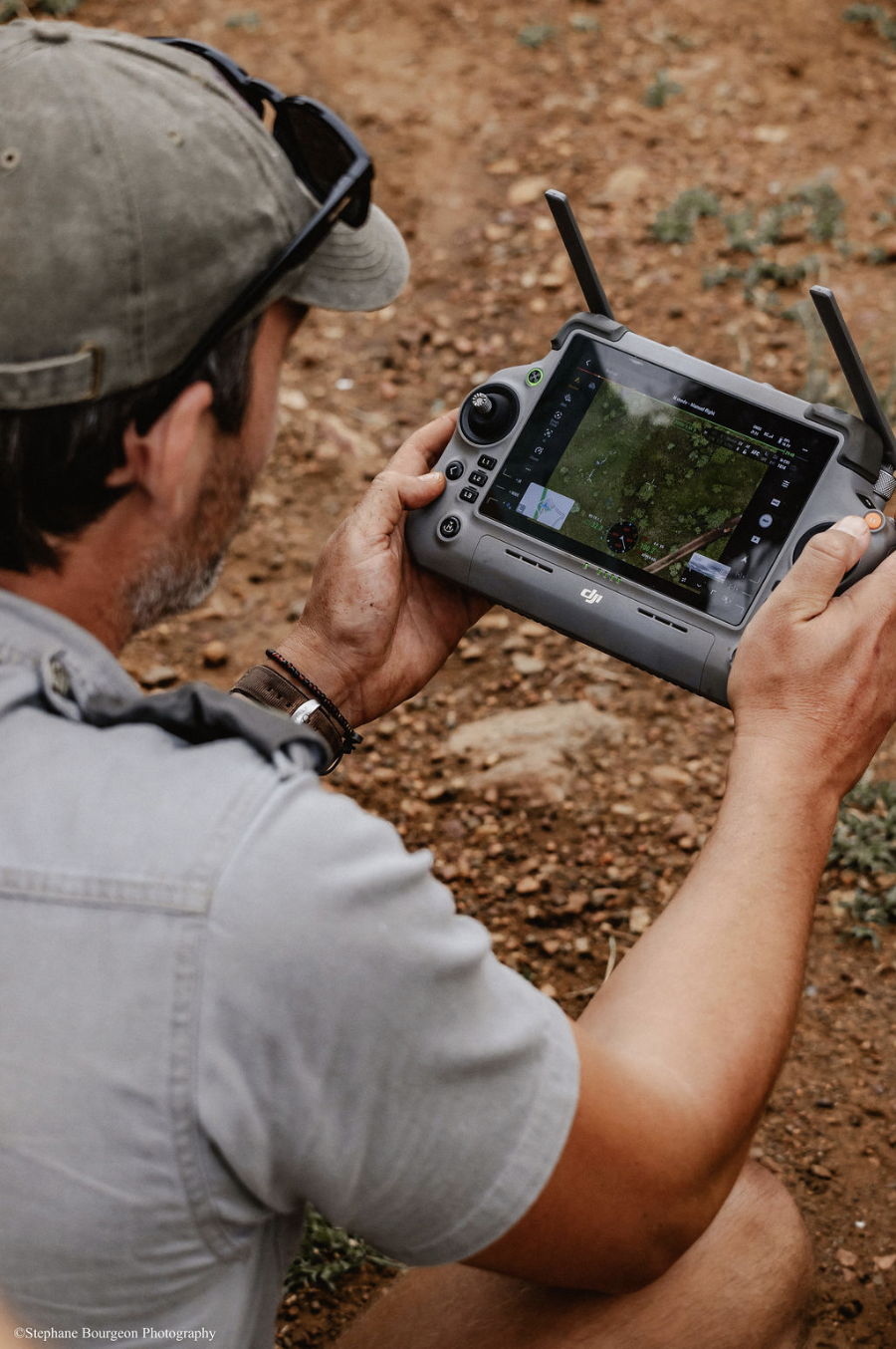 Un homme tenant une télécommande de drone avec un écran affichant une carte et une vue en direct de la caméra du drone, en extérieur en Afrique du Sud.