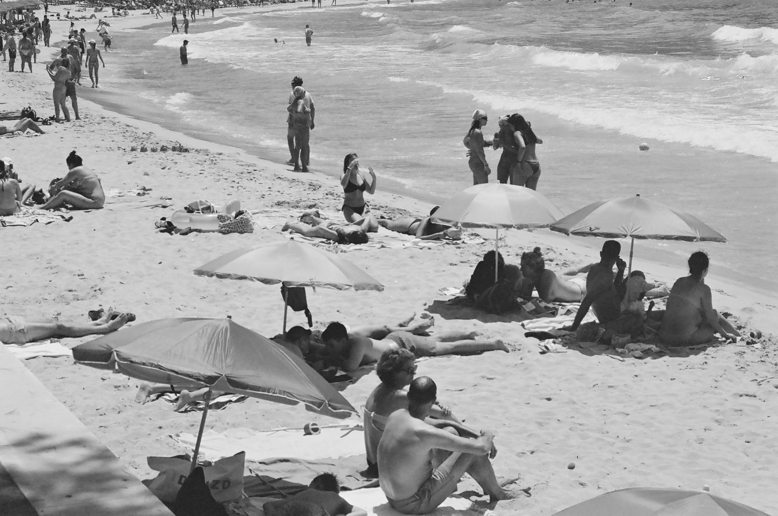 People relaxing and enjoying a day at the beach with umbrellas, on the sandy shore near the water and waves.