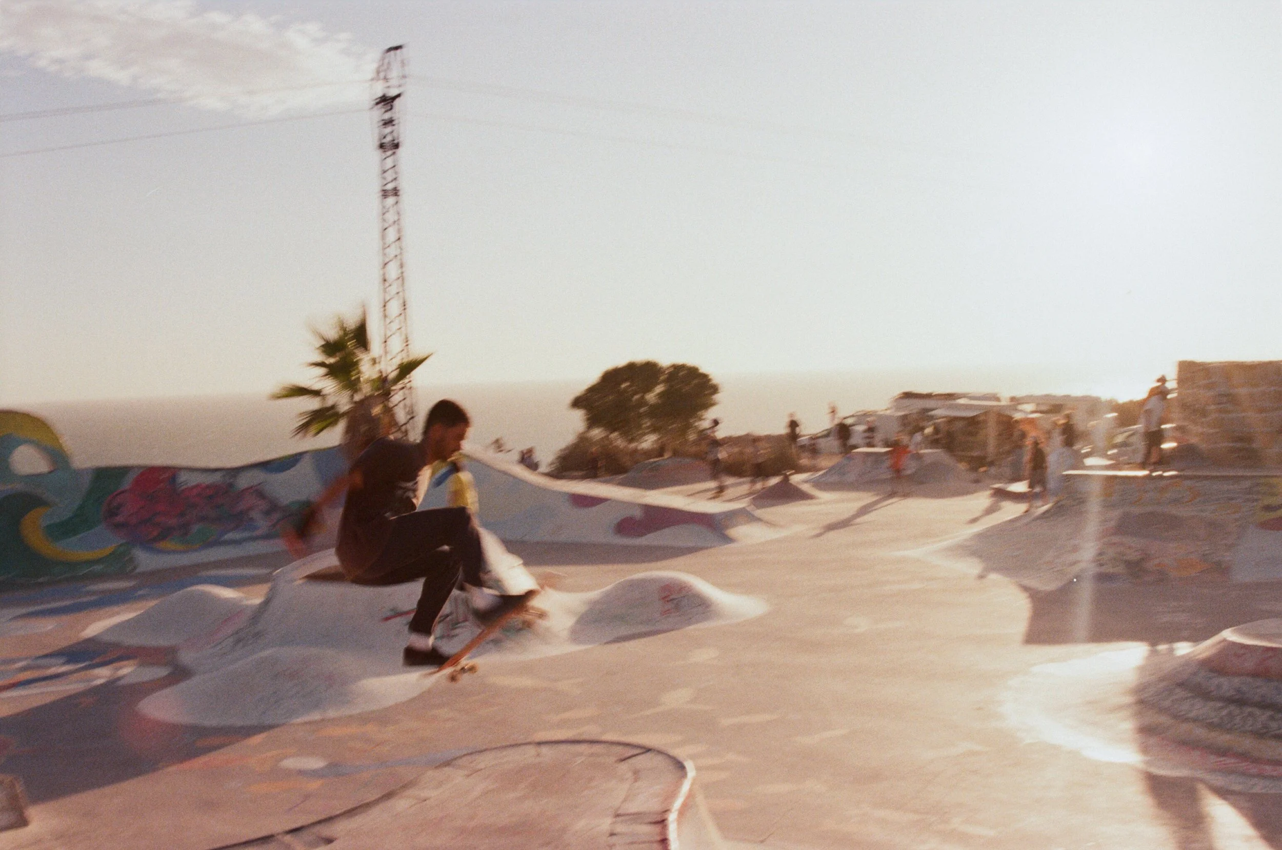 skateboarder performing a trick at a skate park with colorful art on the ramp during sunset.