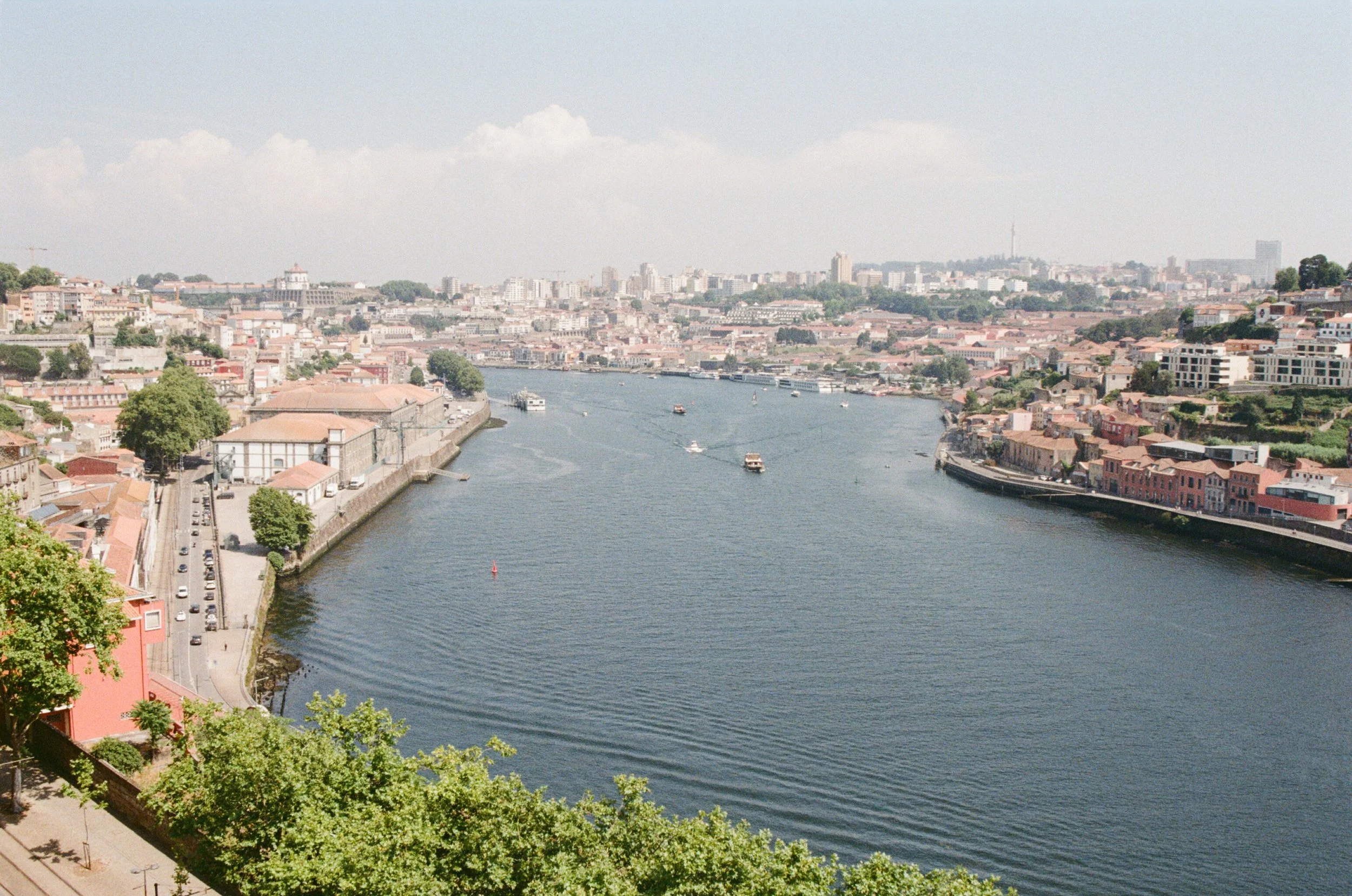 A cityscape view of a river winding through a densely built urban area with boats on the water, historic buildings on either side, and modern high-rise buildings in the distance.
