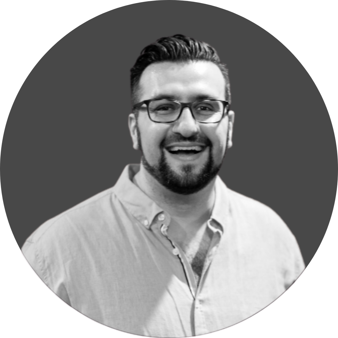 Black and white photo of a smiling man with glasses, short hair, and a beard, wearing a button-up shirt.