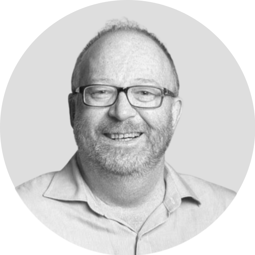 Black and white headshot of a man with glasses, a beard, and a smiling expression, wearing a collared shirt.