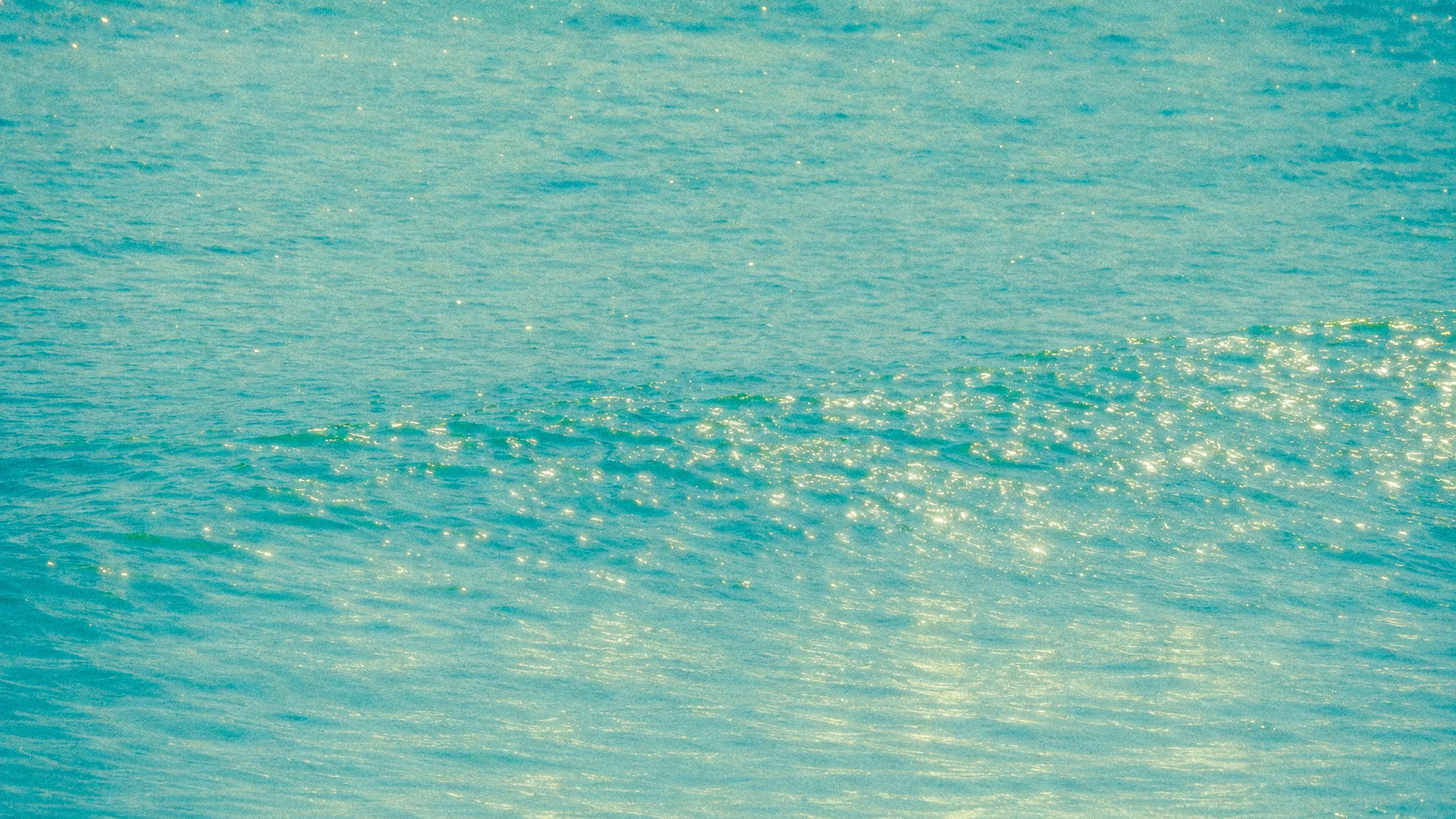The image shows a calm body of water, likely a sea or ocean, with gentle ripples and sunlight reflecting off the surface.