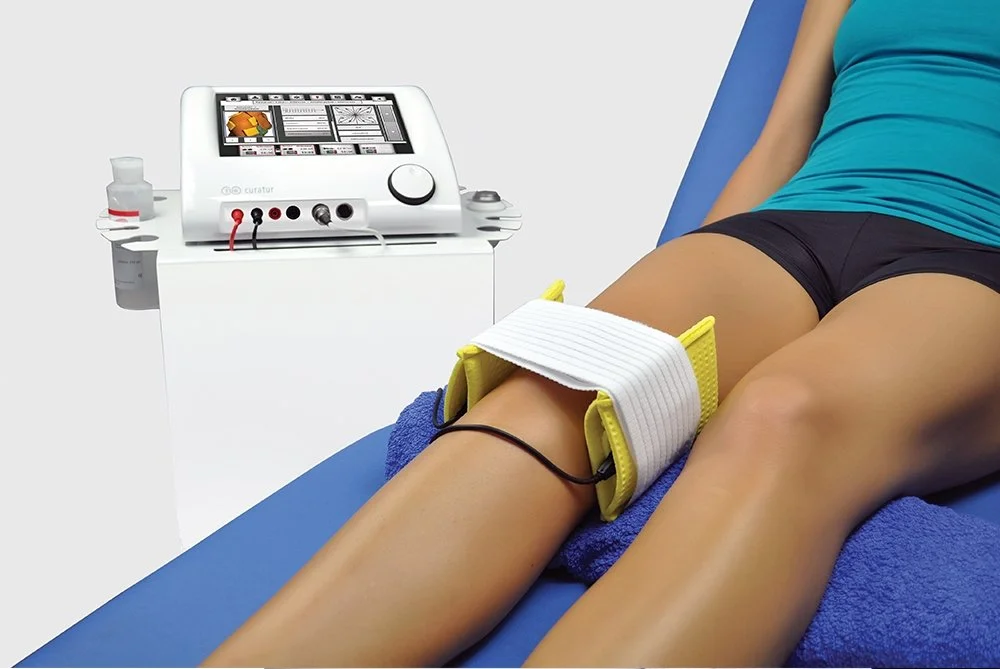 A person undergoing physical therapy with a traction device on their leg, connected to a machine for treatment, lying on a blue treatment table.