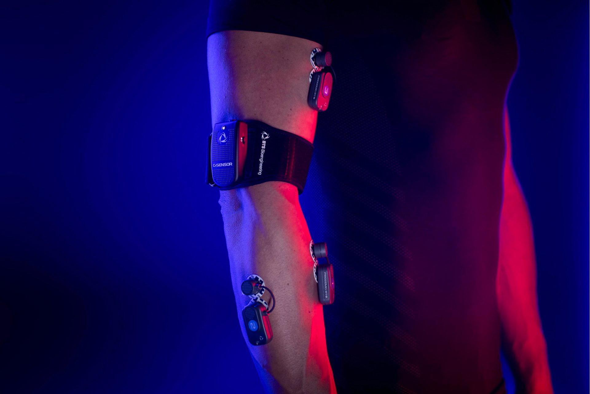 Person's arm with various wearable medical devices attached, illuminated by blue and red lighting.