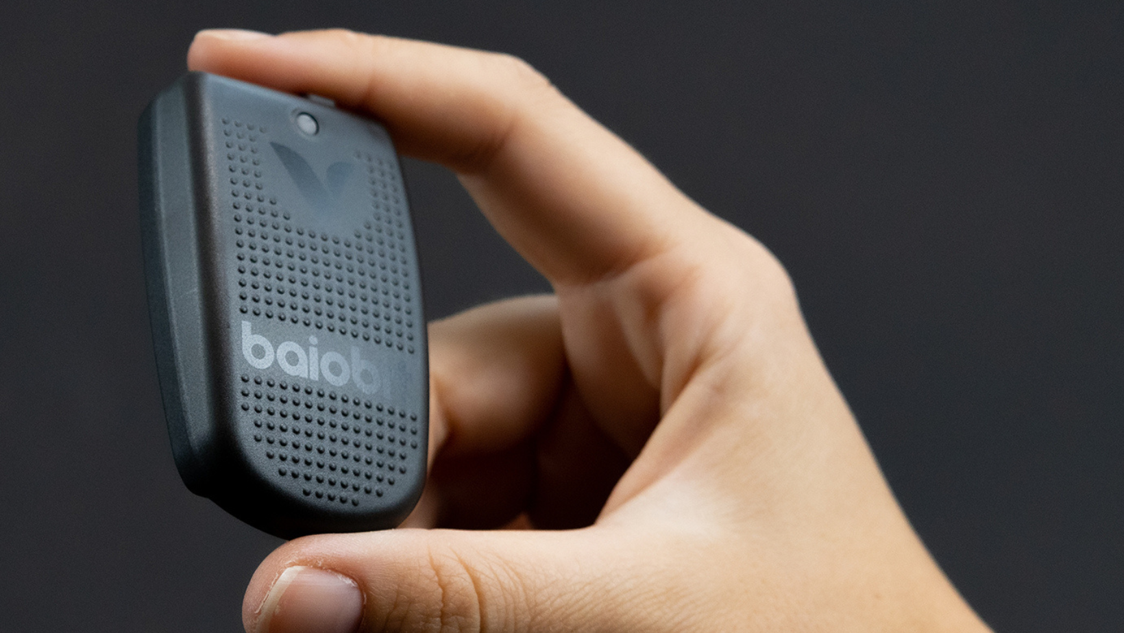 Close-up of a hand holding a small, black, portable device with the brand name 'baib' on it, against a dark background.